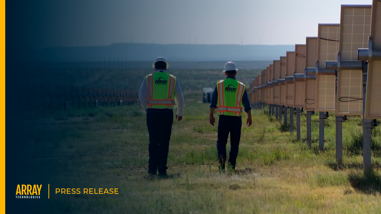 Press release cover image of two workers walking in a field with solar panels lined on the side